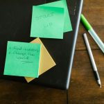Green sticky notes with startup goals on a wooden desk with pens.