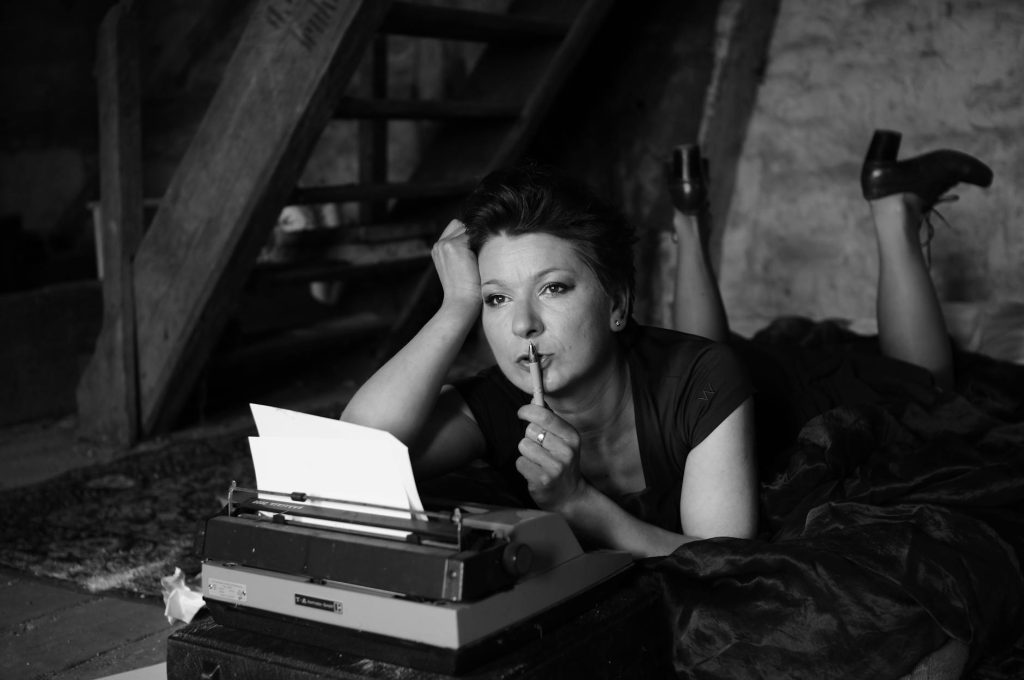 A reflective woman poses elegantly with a typewriter in a black and white setting, evoking nostalgia.