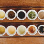 Assorted sauces displayed in bowls on a rustic wooden table.