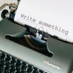 A close-up of a vintage typewriter with 'Write something' typed on paper.