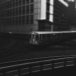 Dynamic black and white photo of a train navigating through a bustling cityscape at night.