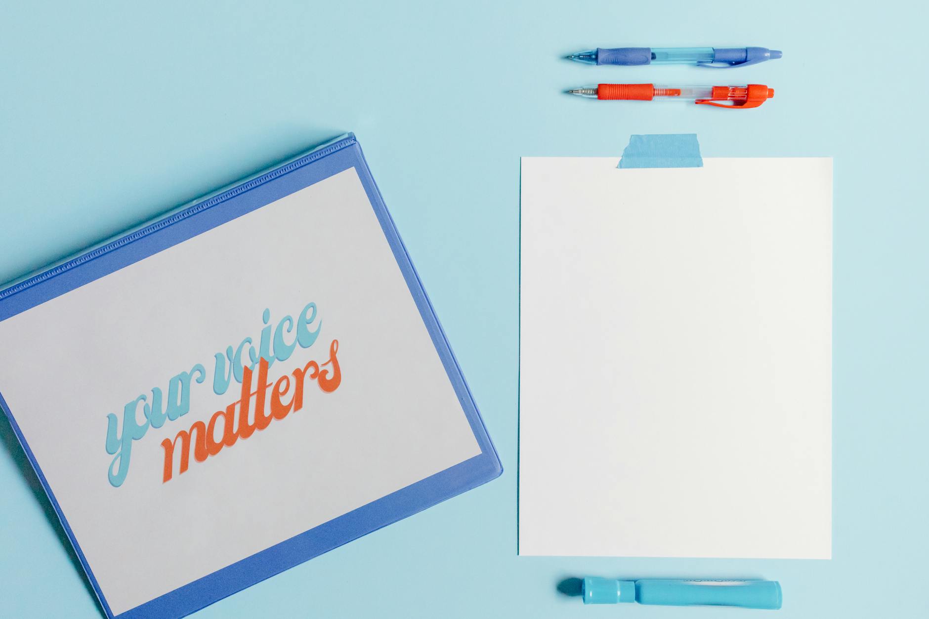 A flat lay of pens, paper, and 'Your Voice Matters' document on a blue background.
