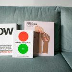 Three design and feminism books displayed on a sofa, highlighting graphic design themes.