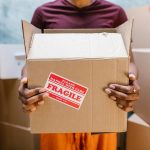 A person holding a cardboard box labeled 'Fragile' during a moving process indoors.