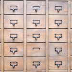 Background of wall full of many similar aged shabby vintage wooden drawers with metal round handles