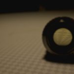 A moody and artistic close-up of a round lens on a patterned surface, cast in shadow.