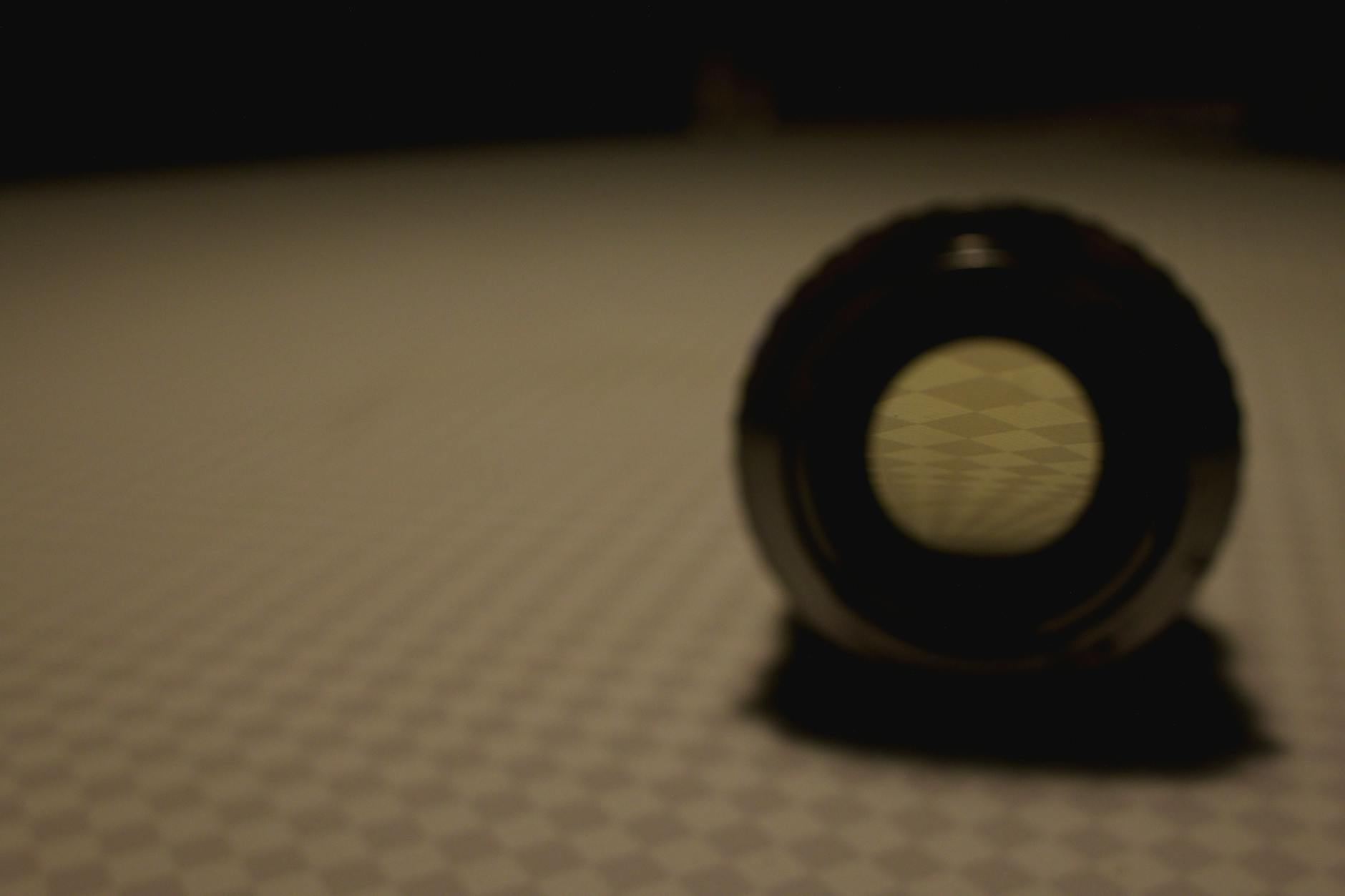 A moody and artistic close-up of a round lens on a patterned surface, cast in shadow.