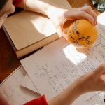Student studying math creatively using an orange and notes in warm indoor light.