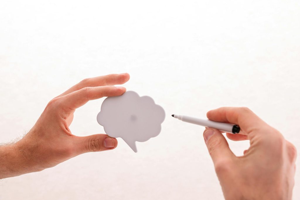 Close-up of hands holding a blank speech bubble with a felt tip pen on a white background.