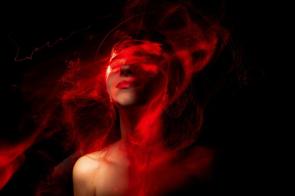 A creative abstract portrait featuring vibrant red neon effects enveloping a human face in darkness.