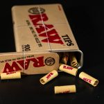 Close-up of RAW pre-rolled tips spilling from a metal tin on a black surface.