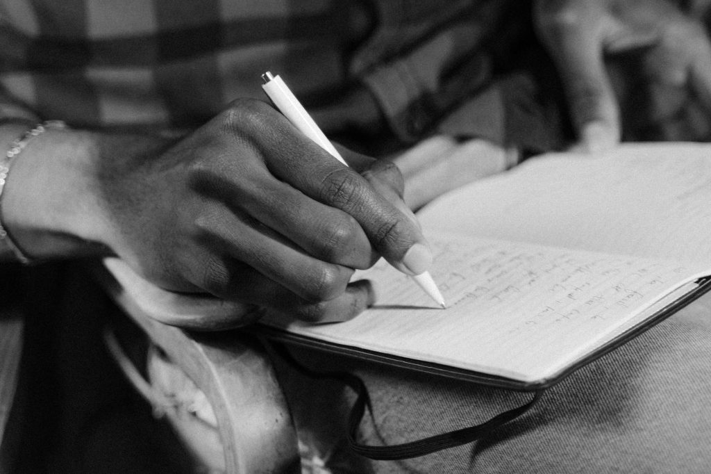 A close-up black and white image of a person writing in a notebook, capturing the essence of expression.