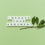 Scrabble tiles spelling 'Improve Your Argument' on a green background with leaves.
