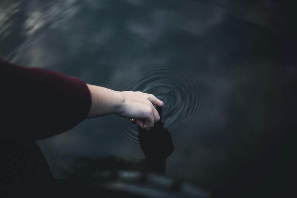 Close-up of a hand gently touching water, creating ripples in a serene setting.
