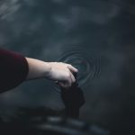 Close-up of a hand gently touching water, creating ripples in a serene setting.