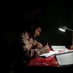 A young man intensely studies under a desk lamp, highlighting focus and determination.