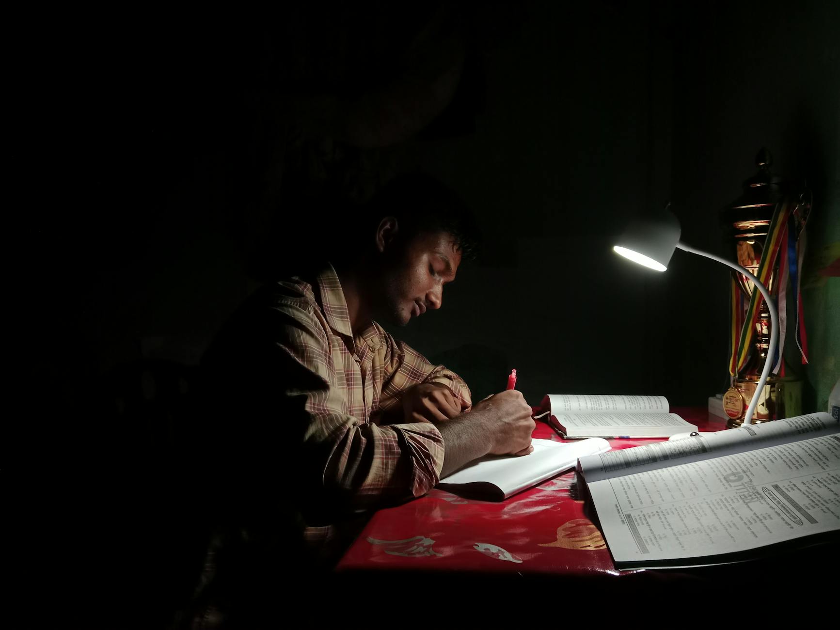 A young man intensely studies under a desk lamp, highlighting focus and determination.
