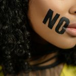 Close-up of a woman with 'No' painted on her face, conveying a powerful message.