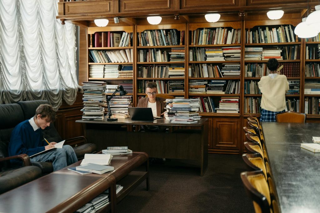 Students studying in a spacious library, surrounded by wooden shelves filled with books.