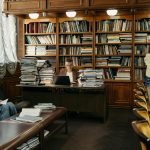 Students studying in a spacious library, surrounded by wooden shelves filled with books.