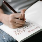 Person writing in a notebook with elegant handwritten calligraphy.