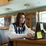Young woman intensely studying on laptop in a university library setting.